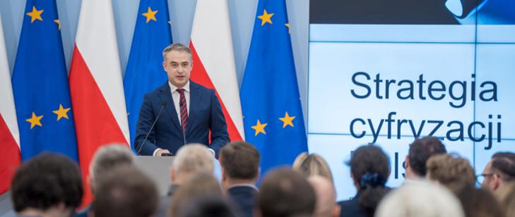 Minister Cyfryzacji K. Gawkowski na tle flag Polski i UE oraz slajdu z napisem Strategia cyfryzacji